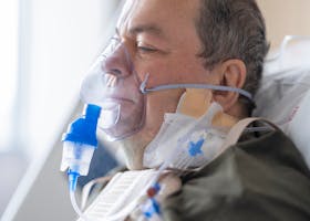 A senior adult patient using an oxygen mask in a hospital setting for medical care.