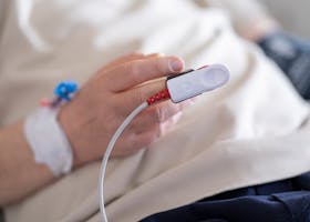 Detailed image of a patient's finger with a pulse oximeter in a hospital setting.