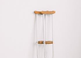 Steel crutches with wooden crossbar and handle leaned on plain white wall in hospital in daytime