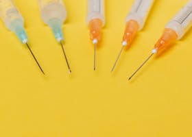 From above of medical plastic disposable syringe injectors sharp needles with orange and green needle hubs and without protective covers on bright yellow surface