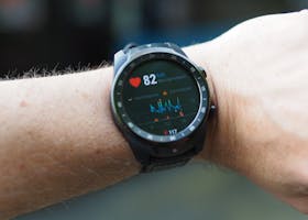 Close-up of a smartwatch showing heart rate and data on a person's wrist outdoors.