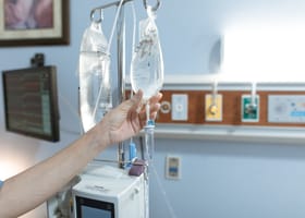 Close-up image of an IV drip and hand in a hospital room, illustrating medical care.
