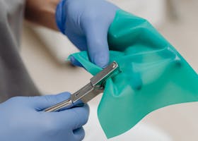 Gloved hands holding medical tool and green drape, highlighting precision in healthcare.