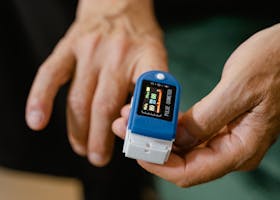 Close-up of a hand holding a blue pulse oximeter measuring oxygen levels and pulse rate.