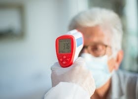 A healthcare professional uses a digital thermometer to check a senior patient's temperature indoors.